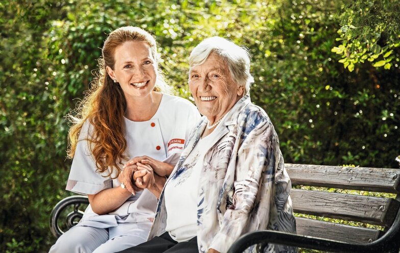 Kursana care provider Caregiver sits with senior on a bench